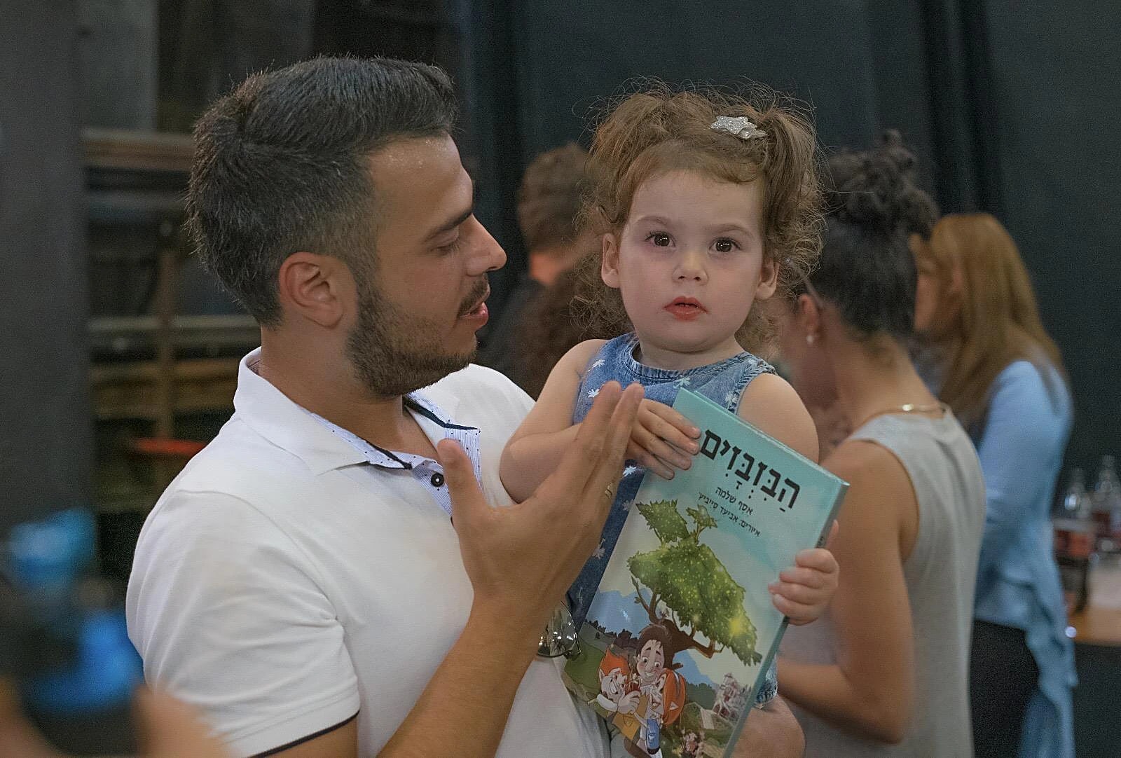 אסף שלמה מחזיק ילדה קטנה שאוחזת בעותק של הספר הבזבזים
